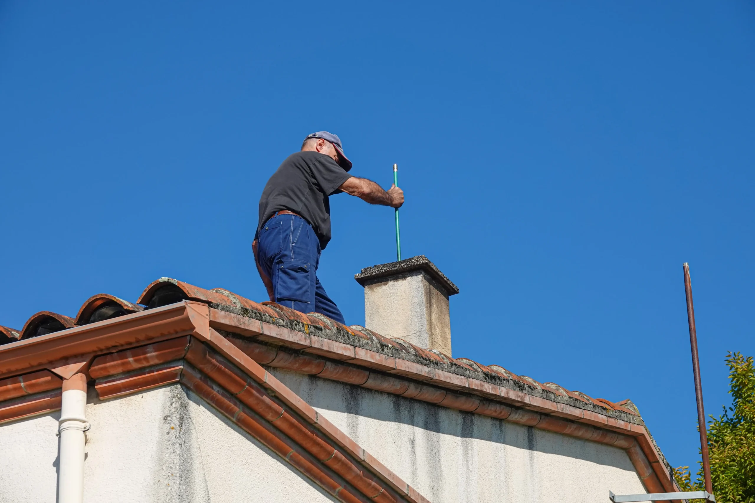 worker on roof cleaning home chimney